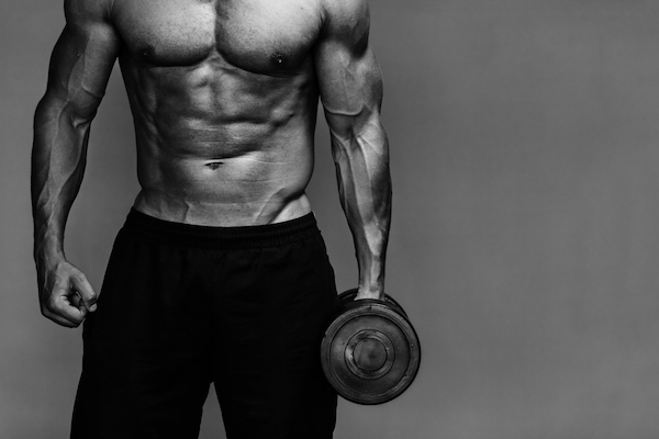 Close up of muscular bodybuilder guy doing exercises with weights over grey background. Black and white